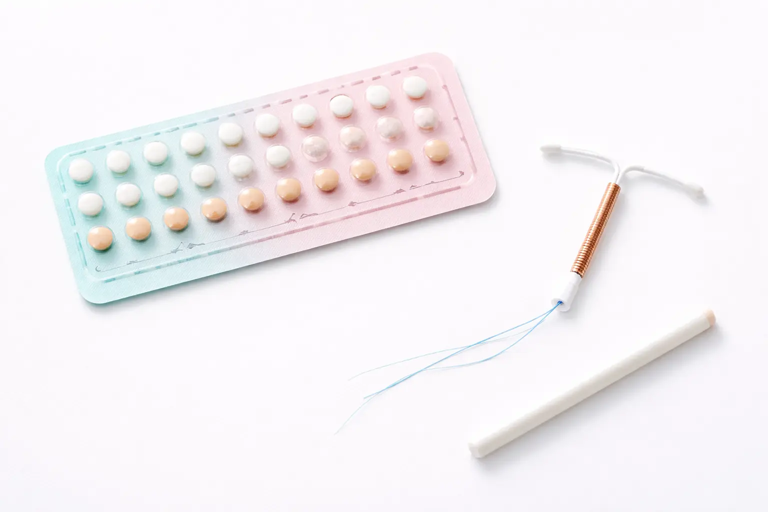 A clean medical flat-lay showing various contraceptive options including birth control pills and an IUD coil