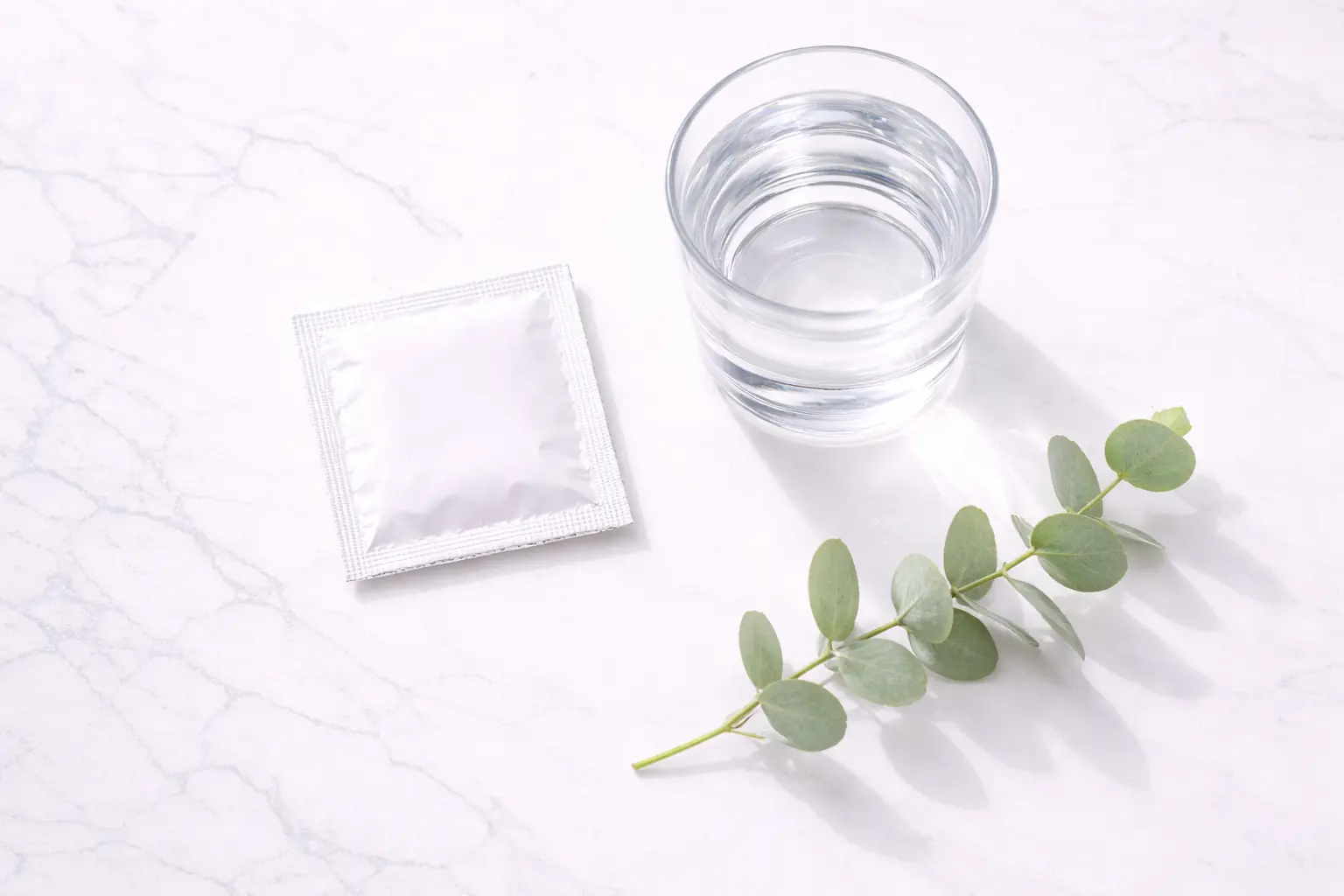 A minimalist flat-lay showing a generic square foil wrapper (condom) and wellness items, representing safe sex and protection