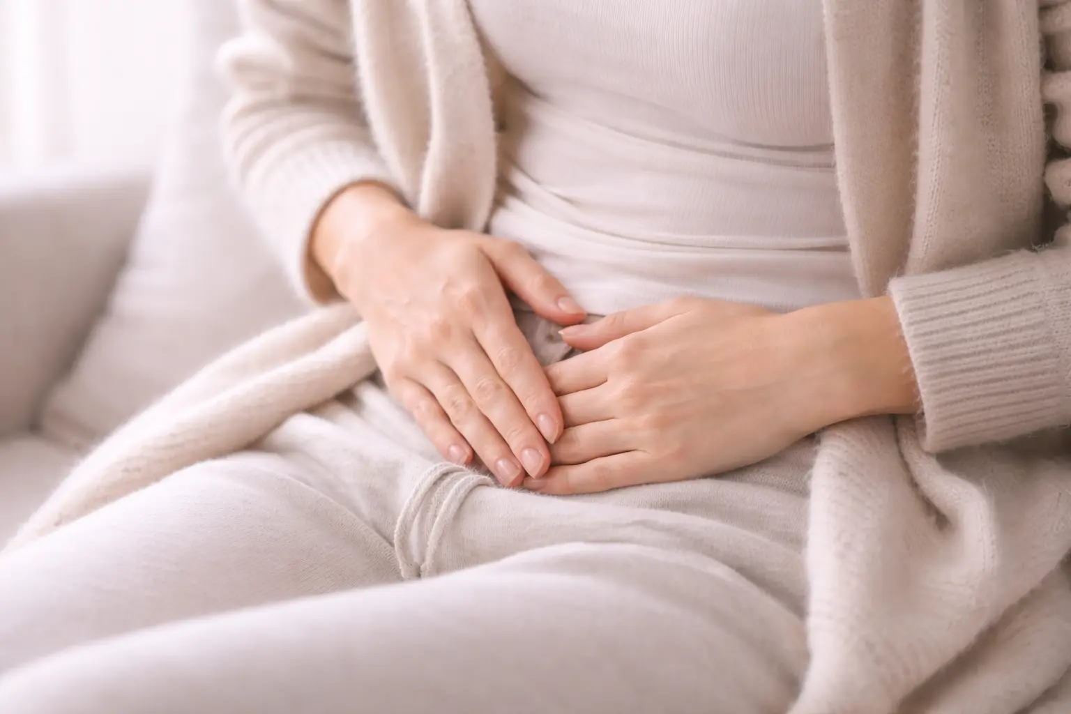 Close-up of a woman’s hands gently pressing on her lower pelvic area to soothe chronic pain