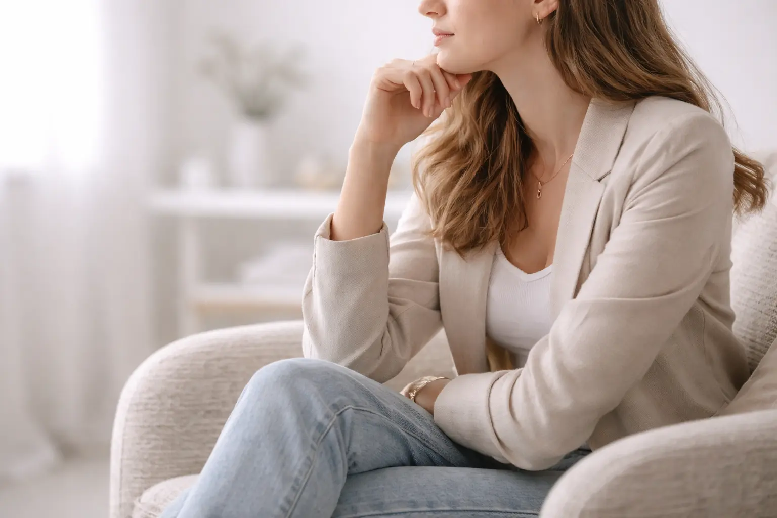 A young woman sitting thoughtfully in a modern chair, reflecting on early menopause diagnosis and health