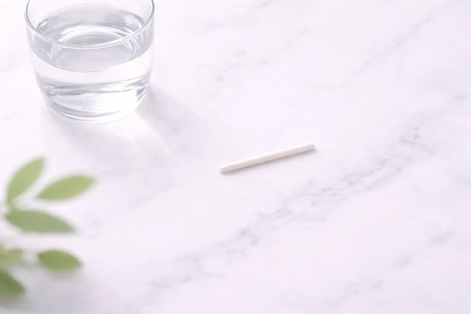 A high-end minimalist flat-lay showing a small, flexible white contraceptive implant rod on a clean surface